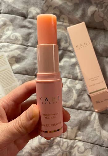 Hand holding a Kahi Wrinkle Bounce Multi Balm against a background with its packaging