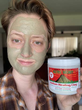 reviewer wearing the clay face mask and holding up the mask tub