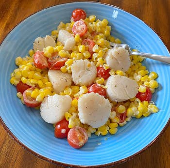 A plate containing scallops, corn, and cherry tomatoes, suggesting a summery seafood dish