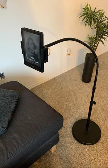 Adjustable floor-standing tablet holder by a couch, displaying 