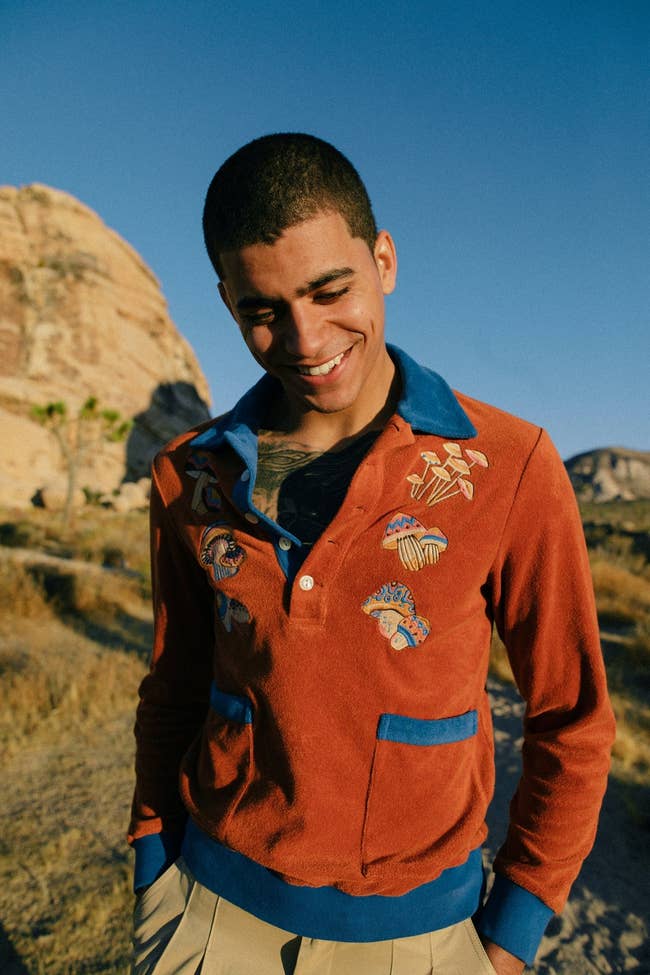 model wearing an orange long-sleeve terry cloth shirt with blue hems and mushrooms embroidered on it