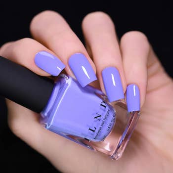 Person holding a vessel  of nail polish, displayed connected  manicured nails matching the lilac polish color