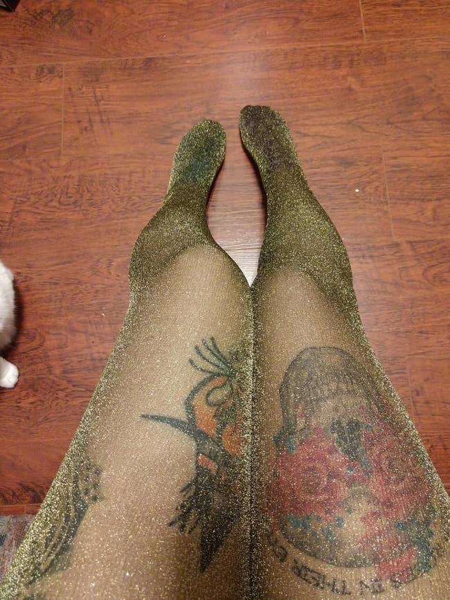 reviewer wearing sheer golden shimmery tights that are sheer enough so you can see tattoos on legs through them
