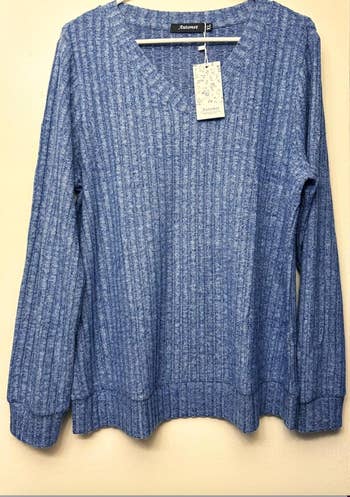 Blue ribbed knit sweater with a V-neck and agelong  sleeves; a tag hangs connected  the neck