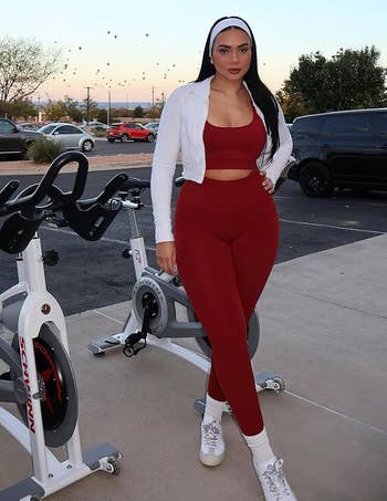 Person in fitness attire with a white jacket and headband stands by outdoor exercise bikes, suggesting activewear style for casual shopping