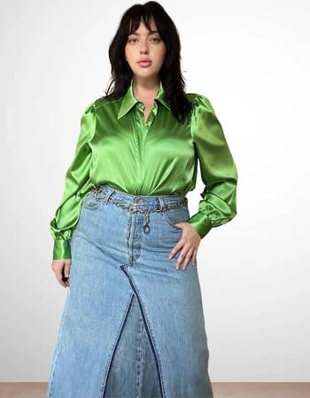 Model in satin blouse and denim skirt, hands on hips, looking at camera for a fashion shoot