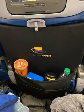 Airplane seat back pocket filled with personal items and a product logo