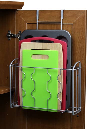 several cutting boards and a muffin pan hung in the over the door basket inside a cabinet