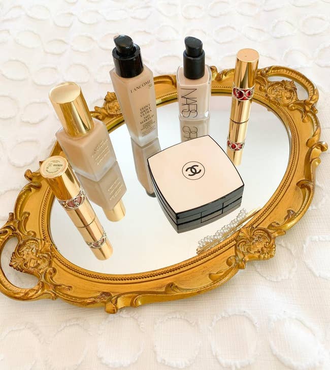 A selection of luxury makeup products, including foundations from Lancome and NARS, displayed on a decorative golden tray