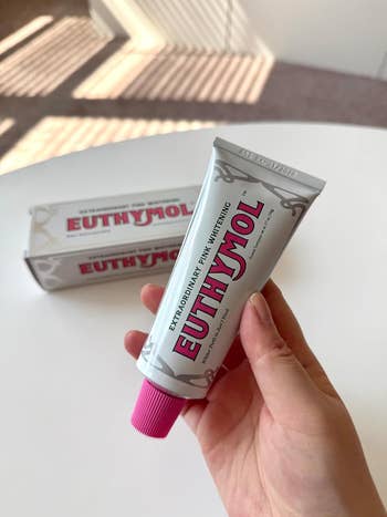 Hand holding a tube of Euthymol toothpaste with a visible box in the background