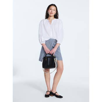 Person in a white blouse and checkered skirt holding a stylish black handbag, wearing black shoes, posing for a shopping article
