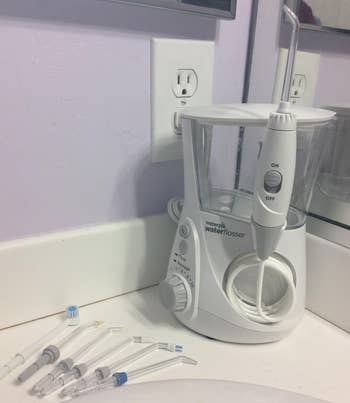 reviewer photo of the white waterpik on a counter next to its various flossing tips