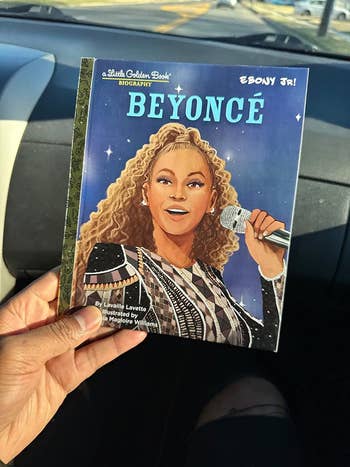 A person holding a children's book featuring an illustration of Beyoncé performing with a microphone