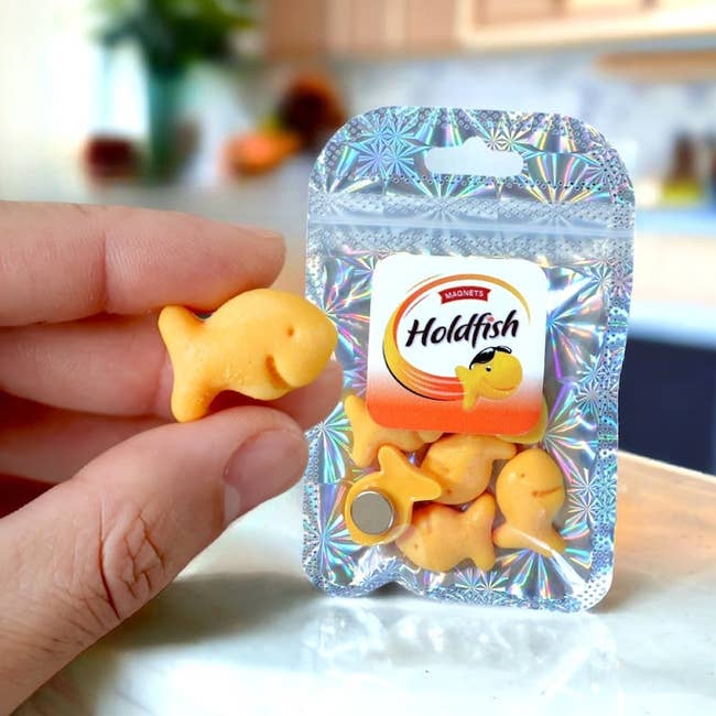 Hand holding a miniature packet of Goldfish crackers with a single cracker in front