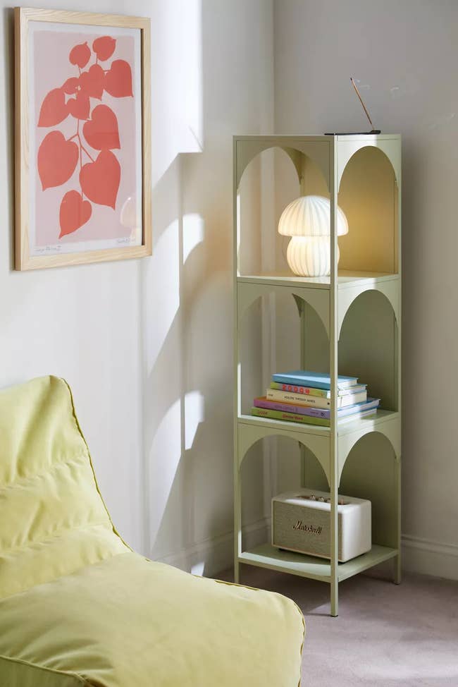 A modern arched shelving unit with books and decorative items next to a green chair