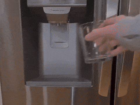 Person filling a glass with water from a fridge dispenser