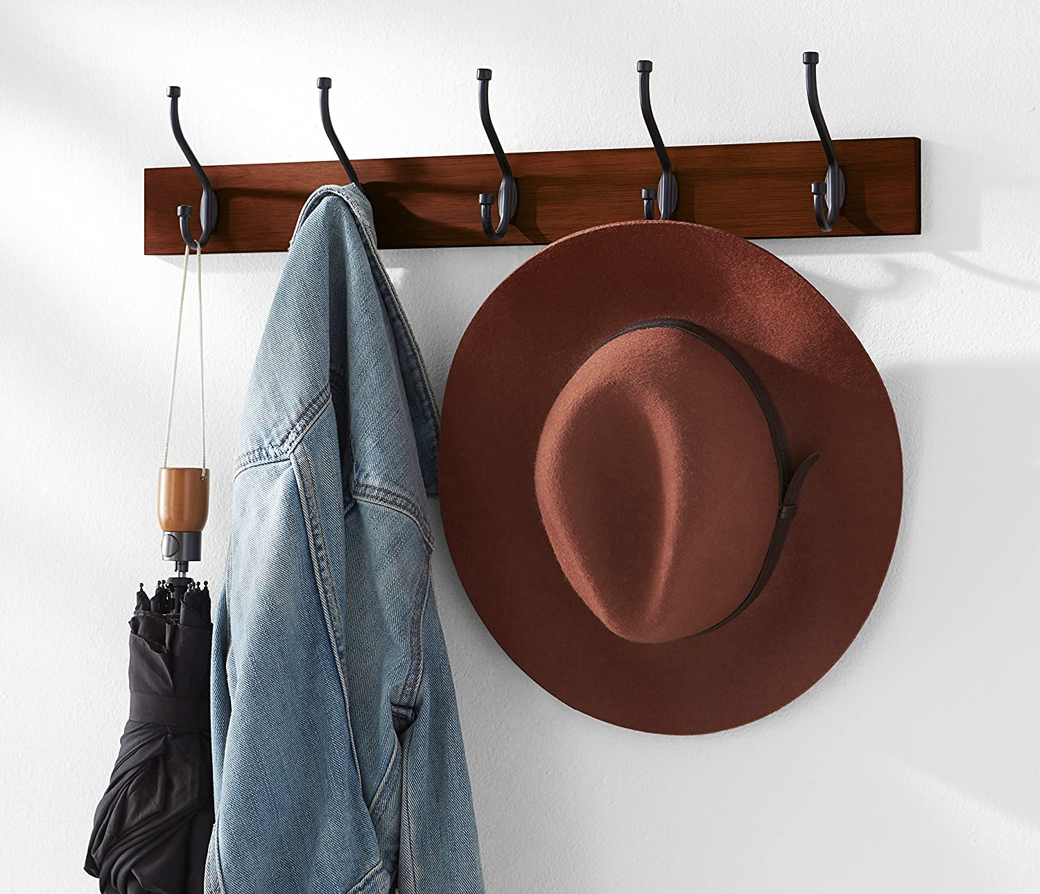 wall mounted coat rack holding a coat, a hat, and an umbrella