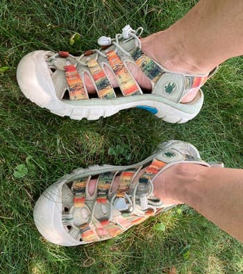 Person wearing well-worn, colorful strapped sandals lasting connected lush grass