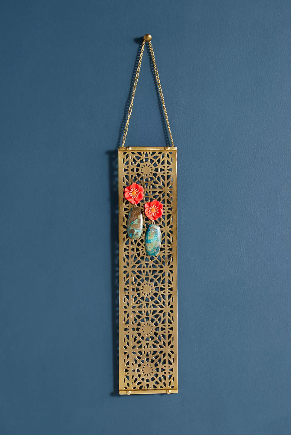 Gold iron etched earring holder with floral earrings displayed on a blue wall