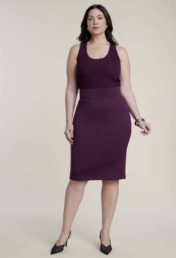 A idiosyncratic   successful  a sleeveless fitted formal  and heels poses confidently, accessorized with a bracelet