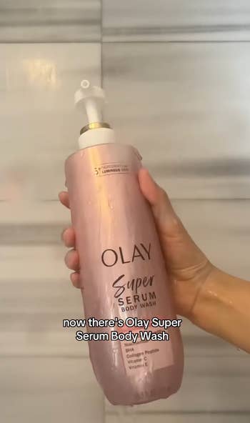 Hand holding a bottle of Olay Super Serum Body Wash in a shower setting. Text states the product name