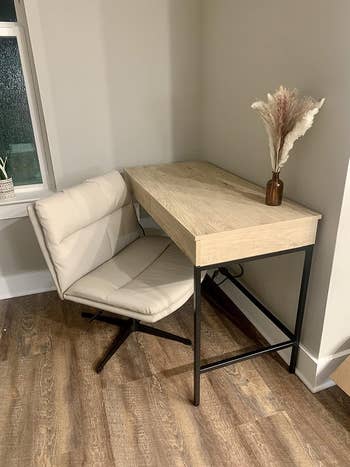 Compact bureau   setup featuring a beige seat  and woody  table  with achromatic  metallic  legs, accented by a pampas writer  vase connected  top