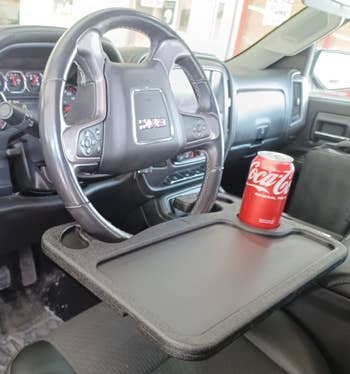 a reviewer photo of the desk mounted on the steering wheel with a soda can on it
