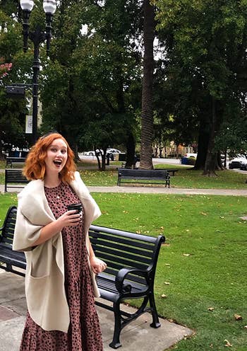 reviewer in a park wearing a polka dot dress with a cream coat, smiling