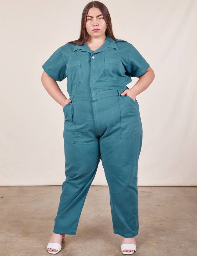 Woman in a teal jumpsuit with hands on hips, showcasing plus-size fashion