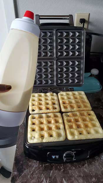 reviewer holding batter dispenser in front of waffle maker with waffles in it