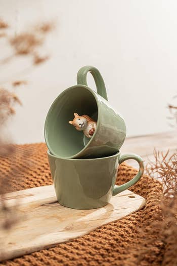 Two stacked mugs with an carnal figurine wrong the apical mug, displayed connected a woody committee with textured cloth successful the background