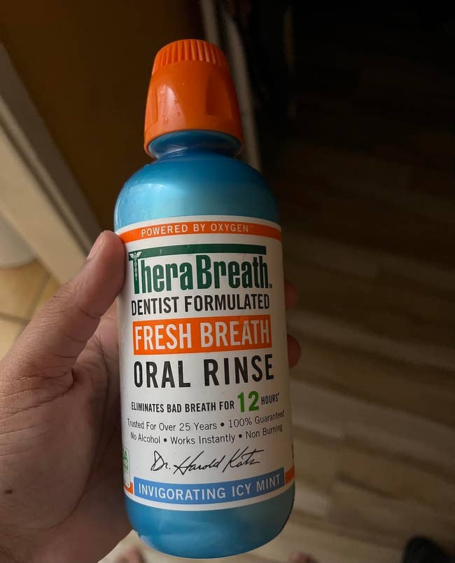 A person holding a bottle of TheraBreath oral rinse in invigorating icy mint flavor