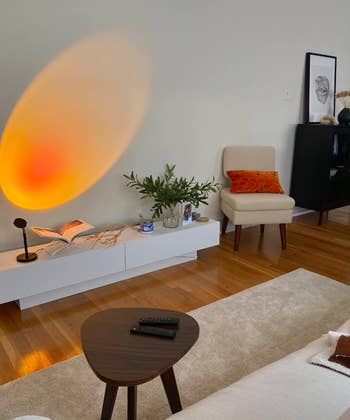 Modern living room with an oval wall light, beige chair with an orange pillow, a plant, and a minimalistic coffee table