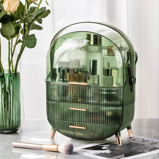 green transparent makeup case with gold details that has three compartments 