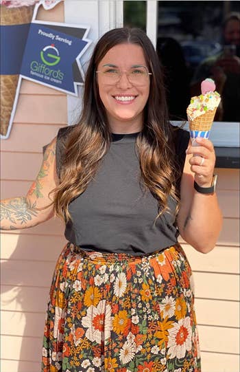 Person smiling and holding an crystal pick cone, wearing a achromatic apical and floral skirt