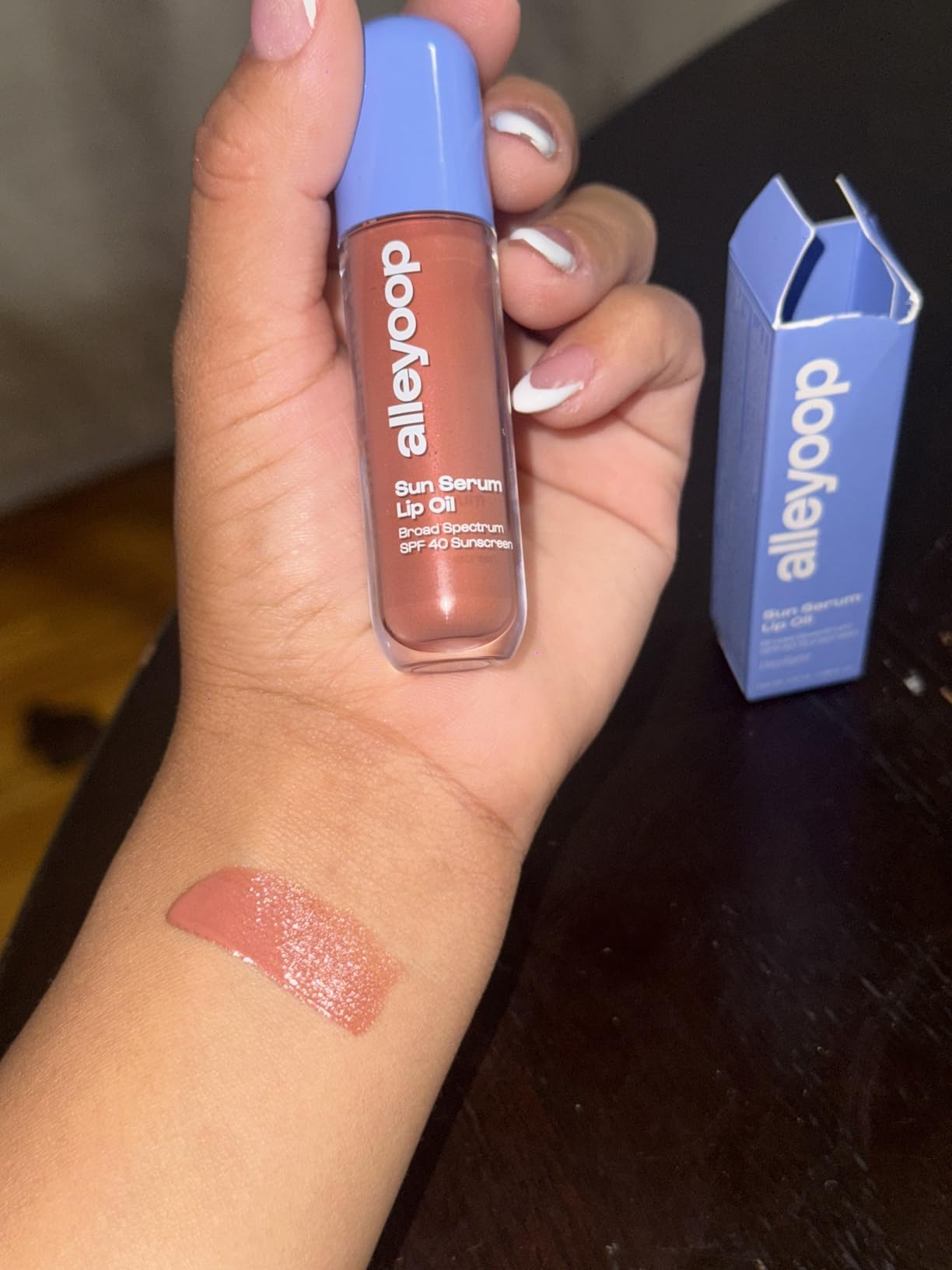 Person holds Alleyoop Sun Serum Lip Oil, with swatch connected  wrist; container  nearby. Featured successful  buying  article