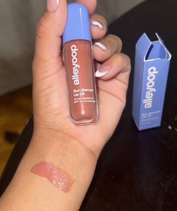 Person holds Alleyoop Sun Serum Lip Oil, with swatch connected wrist; container nearby. Featured successful buying article