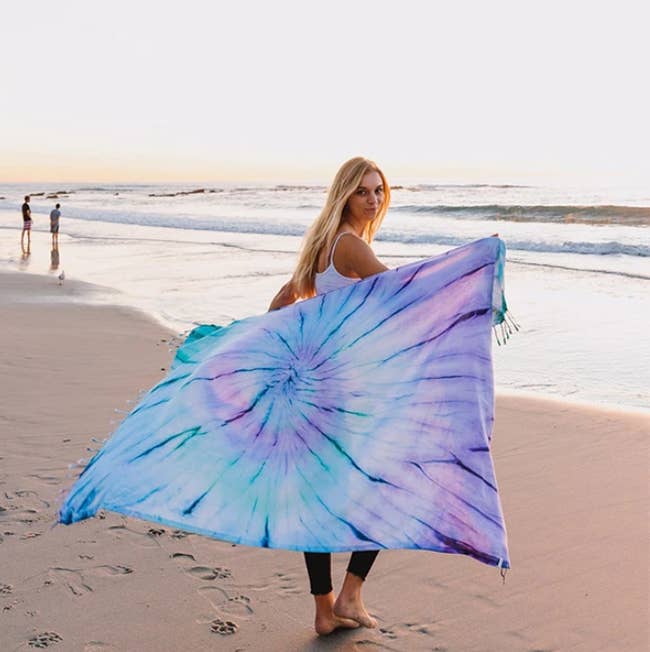 model holding the blue and purple towel while walking on the beach 
