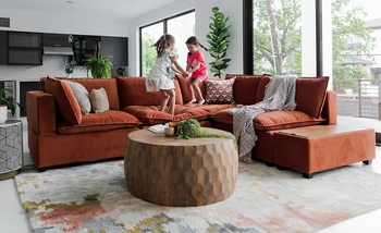 lifestyle photo, two young girls jumping on rust-colored L-shaped couch