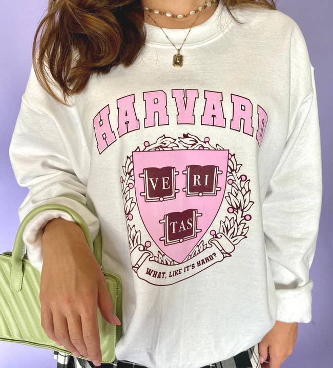 model in white pullover with pink and red harvard logo and text 