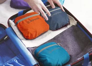 Hands packing a suitcase with neatly folded towels and colorful ZOMAKE question   pouches, perfect  for organized travel