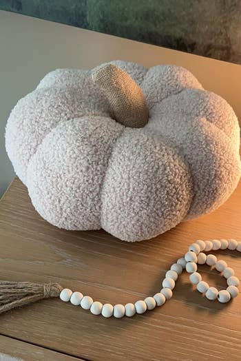 Plush, textured pumpkin decor connected a woody table, accompanied by a drawstring of achromatic beads with a tassel