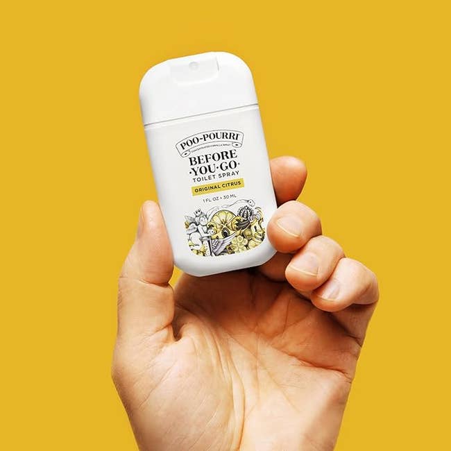 Hand holding a Poo-Pourri toilet spray vessel  against a plain background
