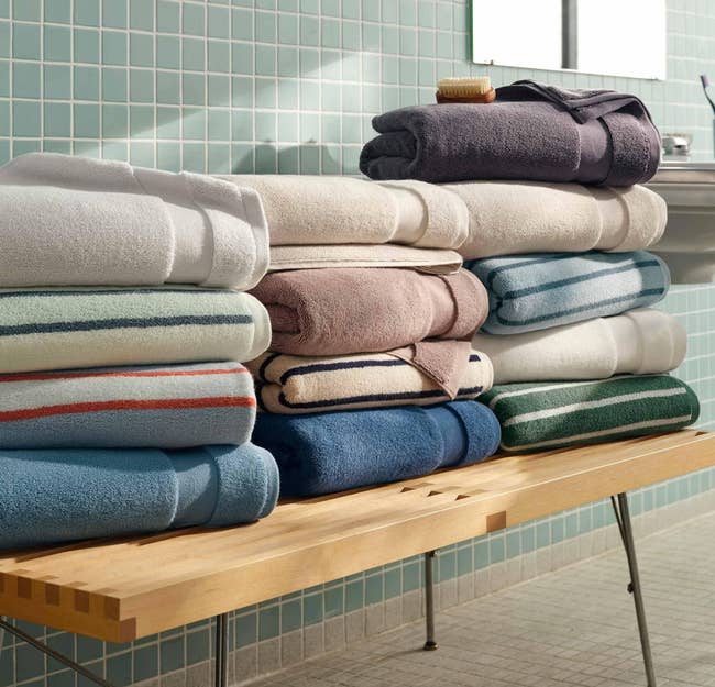 Stack of folded towels successful  assorted  textures and patterns connected  a woody  seat  successful  a bath  with tiled walls