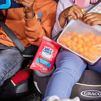 Children in car seats eating snacks with a Wet Ones pack between them