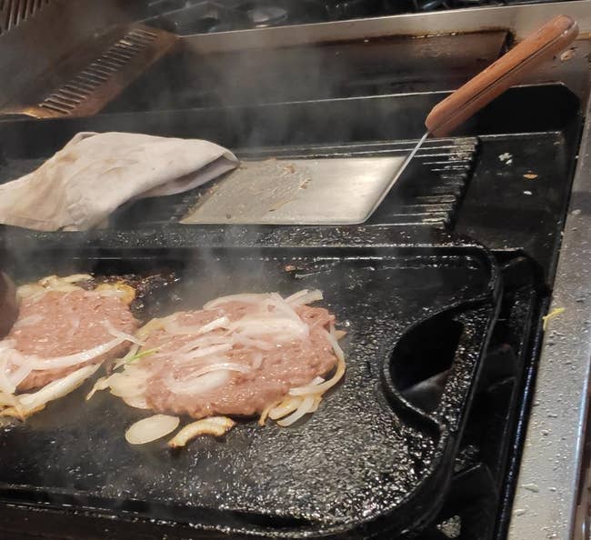reviewer photo of the spatula next to two smash burgers cooking on a griddle