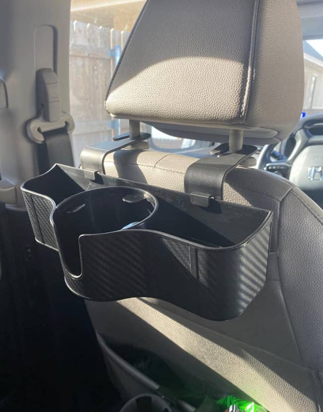 A small black organizer hooked onto the back of a headrest with space for a drink and other accessories 