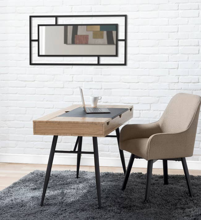Tan upholstered chair with black legs on gray fluffy carpet in front of wooden desk