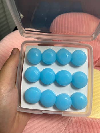 Ten round, blue wax melts in an open plastic container, held in a hand, ready for use