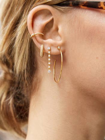 model wearing several of the earrings together in one ear